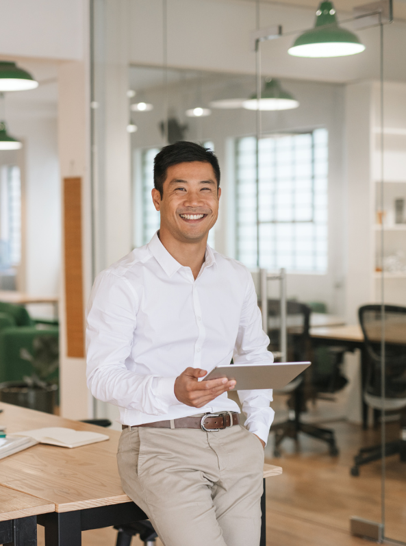 Asian businessman in an office, focused on a tablet PC while seated at a modern desk.